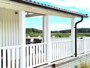 En overdækket terrasse med hvide gelændere, et bord og stole.