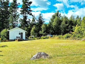 A small white building with a door and windows, surrounded by a grassy field and trees. - 6 Person Holiday Home in Saffle (Saffle)