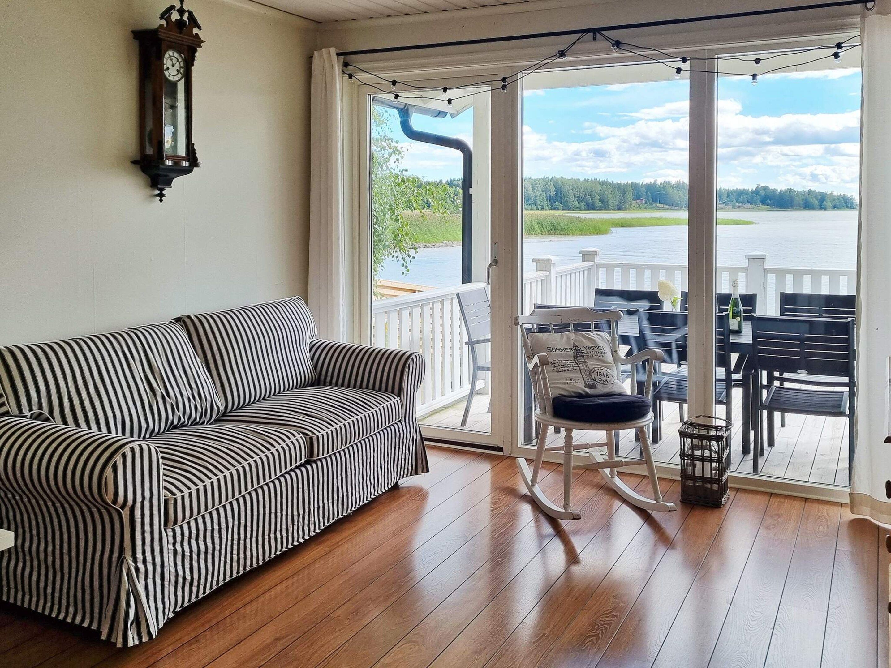 Une pièce avec un canapé à rayures, un fauteuil à bascule et une vue sur un lac, visible à travers une grande fenêtre.