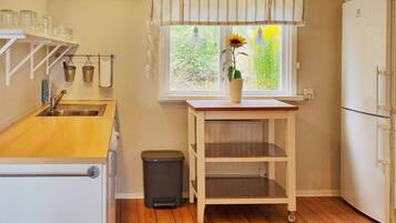 A kitchen with a wooden countertop, a sink, a trash bin, a window with a sunflower, and a refrigerator.