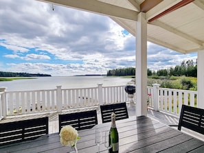A covered outdoor seating area with a view of a lake, a grill, and a bottle of champagne. - 6 Person Holiday Home in Saffle (Saffle)