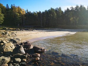Una playa con aguas cristalinas, rocas y un bosque al fondo.