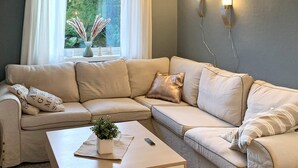 A corner living room with a beige sectional sofa, a small wooden coffee table with a plant, and a window with curtains and a vase of pampas grass. - 8 Person Holiday Home in Bolandet-by Traum (Heroy)