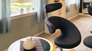 A modern kitchen with a curved black chair, a small table with a white vase, and a view of houses through the window. - 8 Person Holiday Home in Bolandet-by Traum (Heroy)