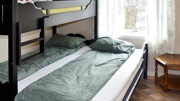 Uma cama beliche com roupa de cama verde, um criado-mudo de madeira e uma janela com cortinas.