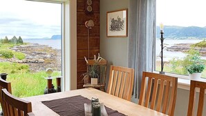 A dining area with a wooden table and chairs, a view of a rocky coastline, a wall-mounted light fixture, and a framed picture. - 8 Person Holiday Home in Bolandet-by Traum (Heroy)
