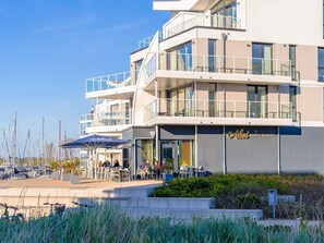 A modern building with multiple balconies, outdoor seating, and a view of the marina.