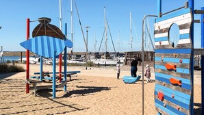 A beach with a climbing structure, a shaded area, and boats in the background.