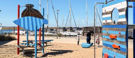 A beach with a climbing structure, a shaded area, and boats in the background.