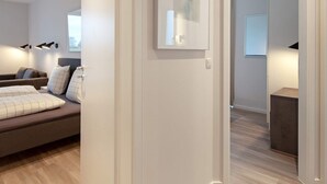 A modern hotel room with a bed, a sofa, a framed picture on the wall, and a door leading to another room.