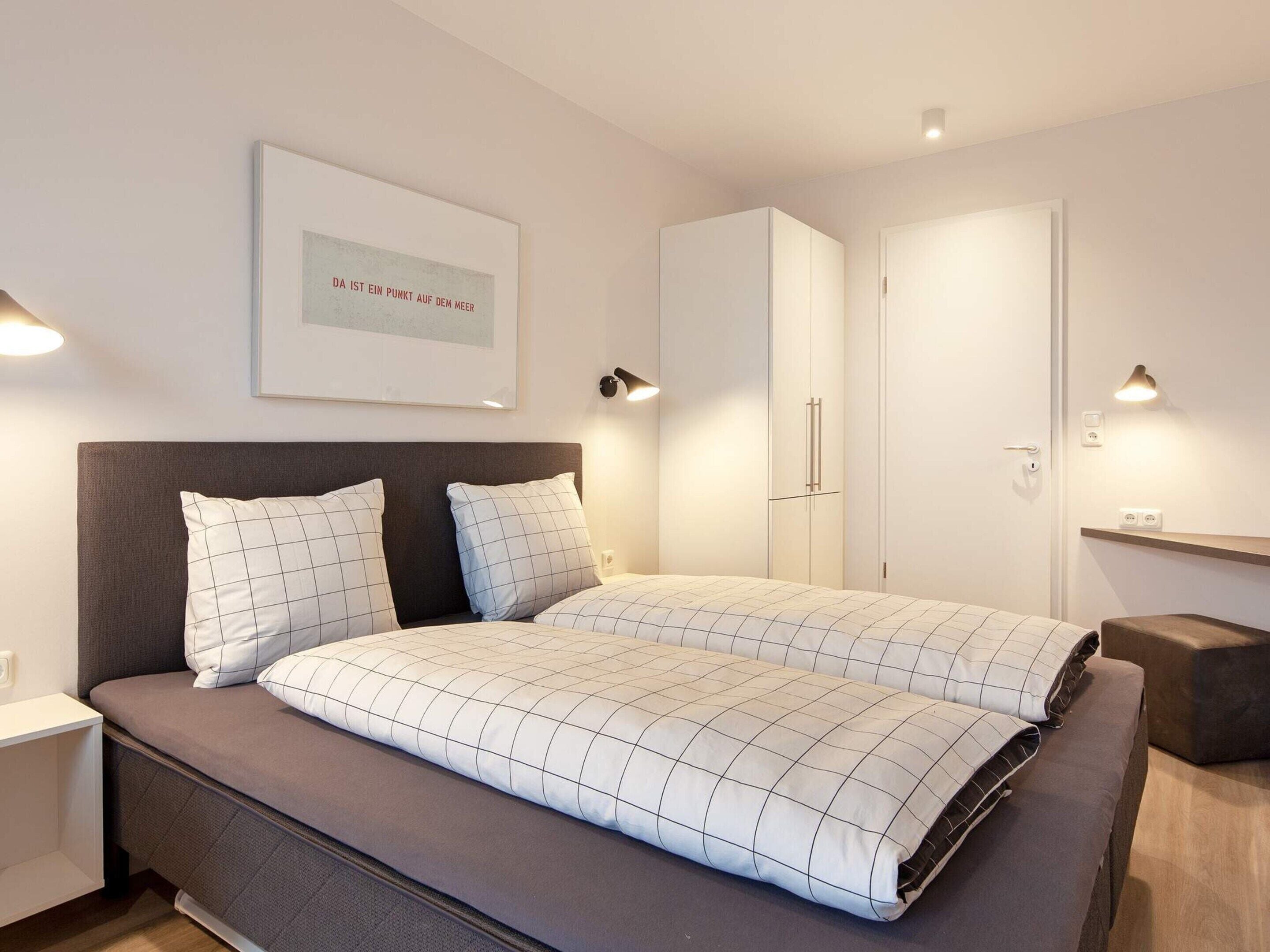 A modern bedroom with a bed, bedside tables, a wardrobe, and a framed picture on the wall.