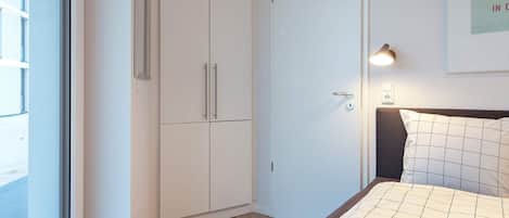 Un dormitorio con cama, armario, puerta, lámpara de pared y un cuadro enmarcado.