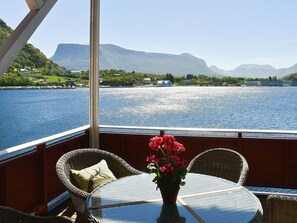 A table with wicker chairs and a glass top, overlooking a lake with mountains in the background. - 8 Person Holiday Home in Midsund (Molde)