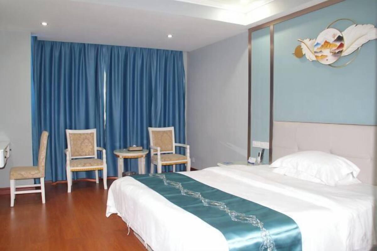 Quarto de hotel com uma cama grande, duas cadeiras, uma mesinha e um espelho na parede.