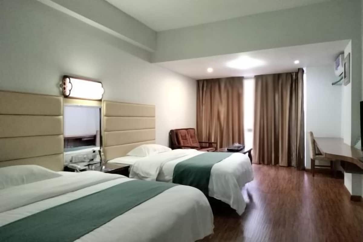 Quarto de hotel com duas camas, uma escrivaninha, uma cadeira, um espelho e uma janela com cortinas.