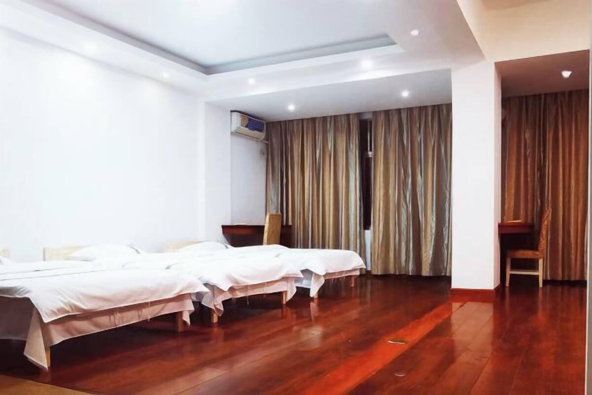 Quarto de hotel com duas camas, piso de madeira, luminária no teto e cortina na janela.
