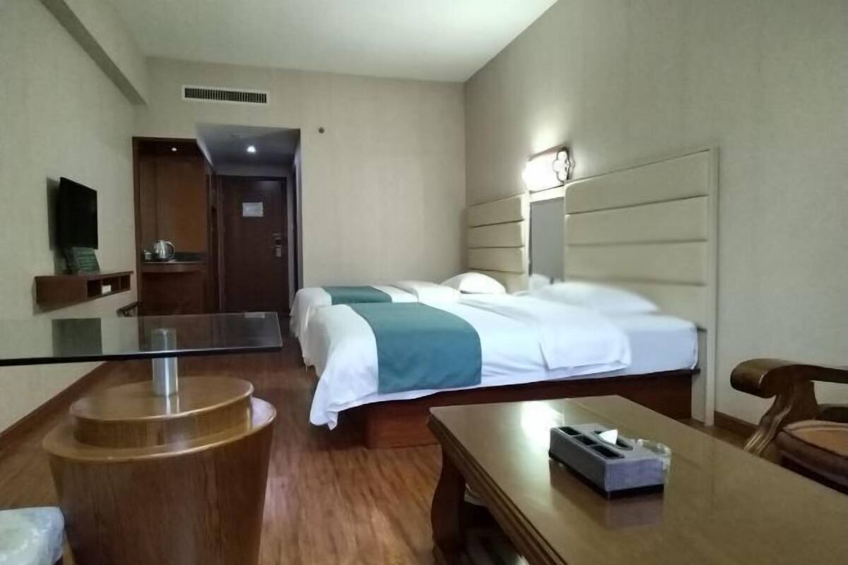 Quarto de hotel com duas camas, uma mesa de madeira, um espelho e um pequeno espaço de estar.