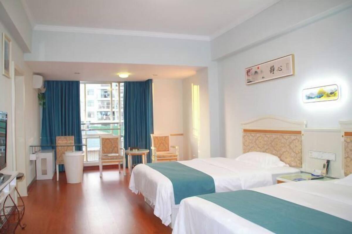 Quarto de hotel com duas camas, uma escrivaninha, uma cadeira e vista para o exterior.