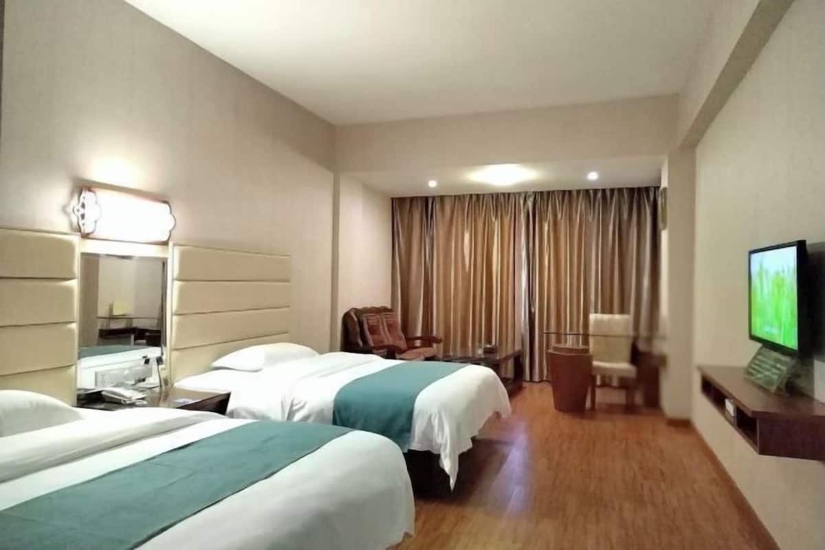Quarto de hotel com duas camas, uma escrivaninha, uma cadeira, uma televisão e uma janela grande com cortinas.