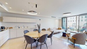 Une cuisine moderne avec des meubles blancs, une table de salle à manger ronde entourée de chaises et une grande fenêtre offrant une vue sur la ville.