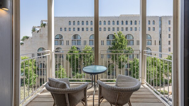 Un balcon avec des fauteuils en osier et une table, donnant sur un immeuble aux fenêtres en arc de cercle.