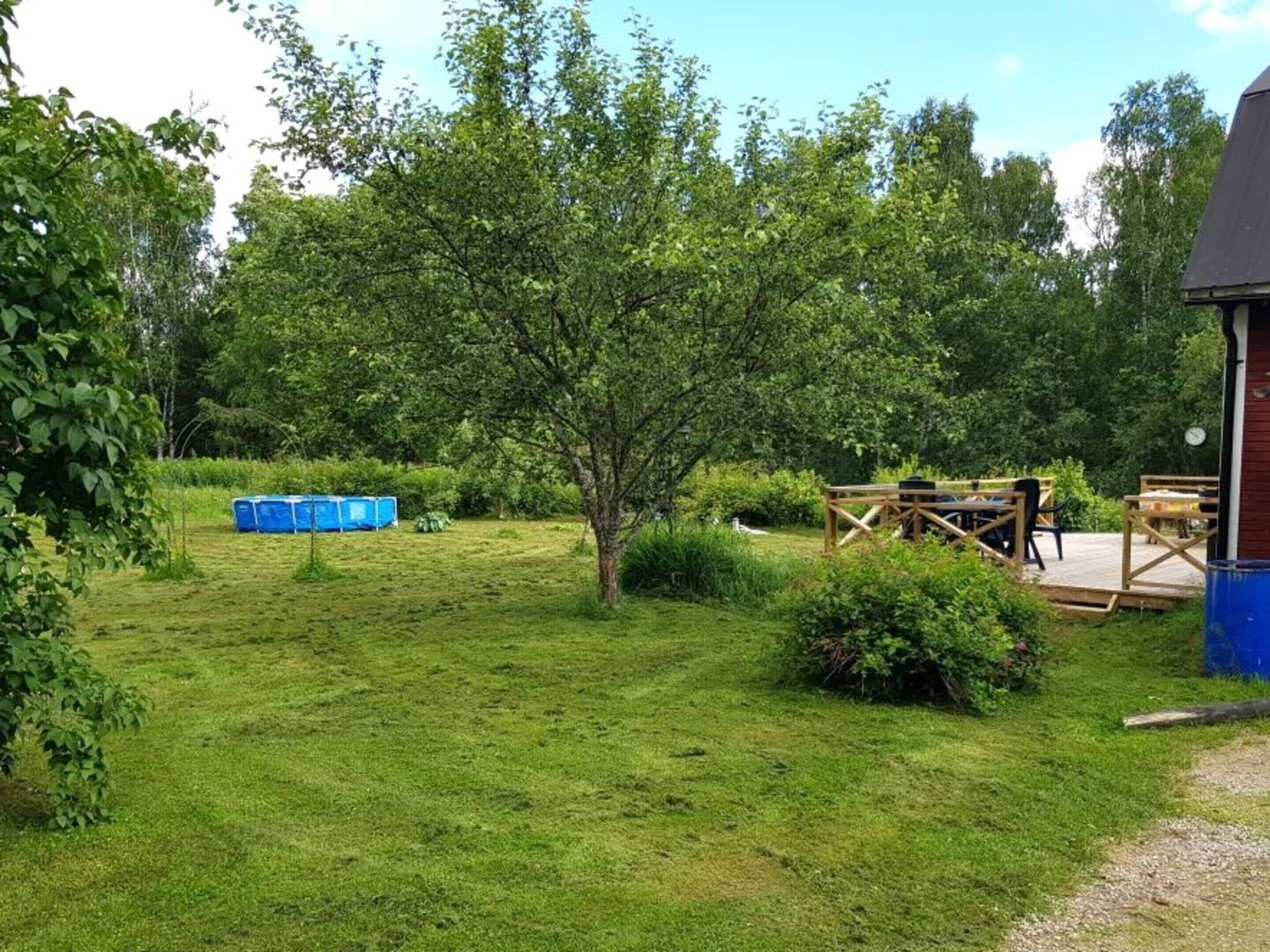 A grassy outdoor area with a wooden deck, picnic tables, and a blue storage shed.