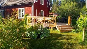A red wooden house with a metal roof, a wooden deck, and a grassy yard.