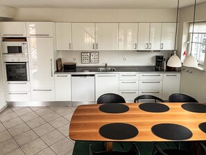 Una cocina moderna con armarios blancos, una mesa de comedor de madera con centros de mesa circulares negros y piso de baldosas.