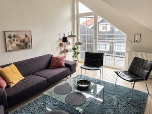 Uma sala de estar moderna com um sofá escuro, uma mesa de centro de vidro e uma cadeira preta.