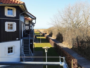 Um edifício de dois andares com uma escadaria que leva a uma varanda, um caminho e vista para a paisagem.