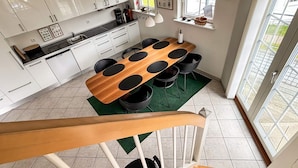A modern kitchen with white cabinets, a wooden dining table with black chairs, a green rug, and a clock on the wall. - 4 Star Holiday Home in Bogense (Bogense)