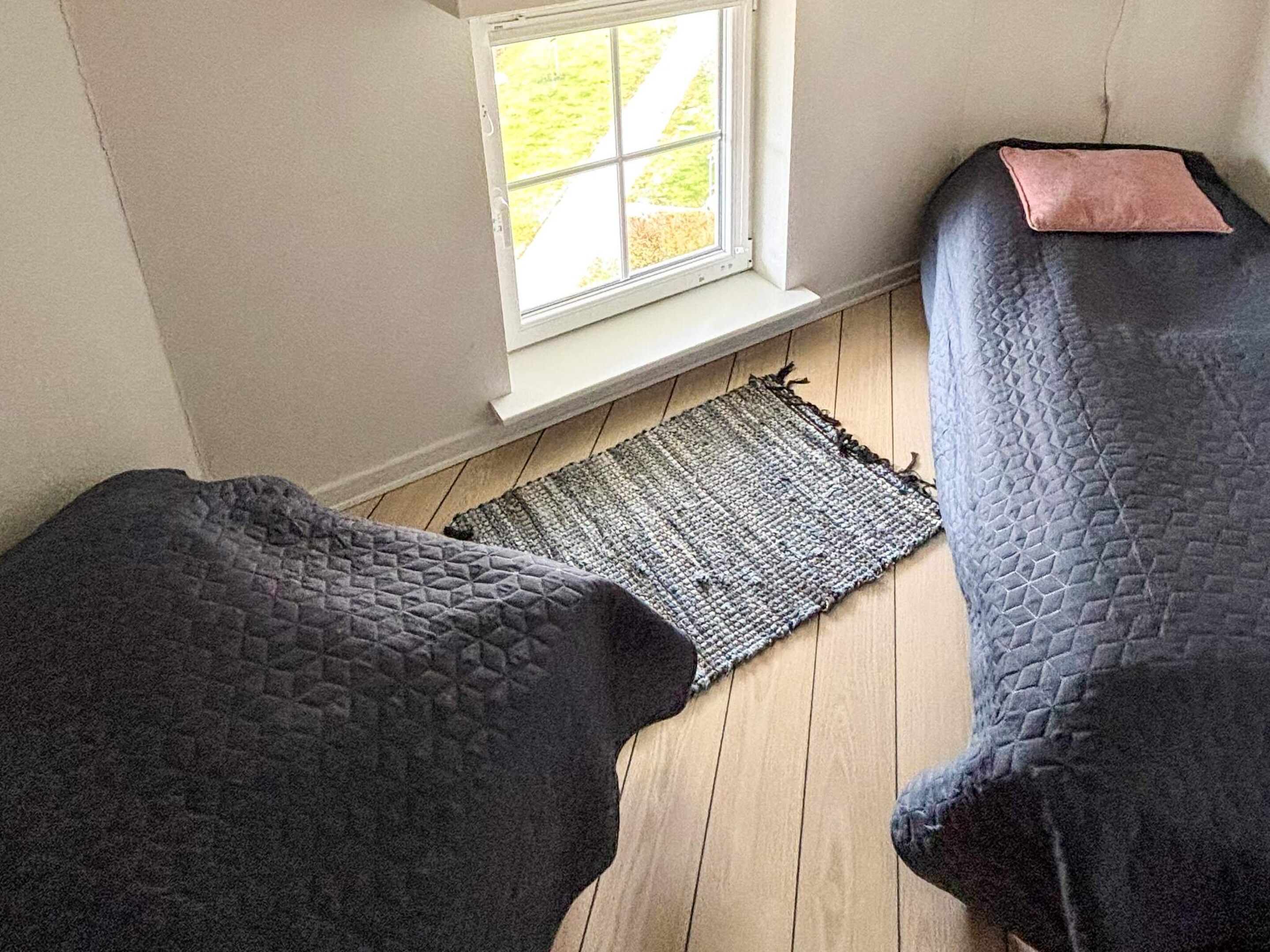 A room with two beds covered in dark blankets, a window with a view of greenery, and a wooden floor.