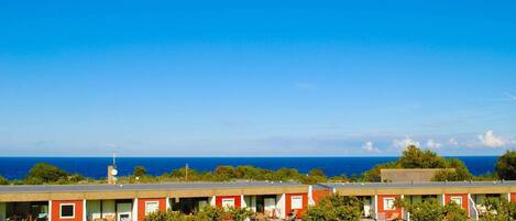 A row of red and white motel buildings with a grassy lawn and trees in front, overlooking a clear blue ocean.
