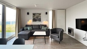 Un salon moderne avec un canapé d’angle, une petite table, un fauteuil, un téléviseur à écran plat et une cheminée.