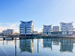 A waterfront property with modern architecture, featuring multiple floors and balconies, and a reflection in the water. - 5 Star Holiday Home in Wendtorf (Wendtorf)