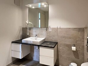 A modern bathroom with a white sink, black countertop, and a large mirror. There are two white cabinets below the sink and a toilet to the right. - 5 Star Holiday Home in Wendtorf (Wendtorf)
