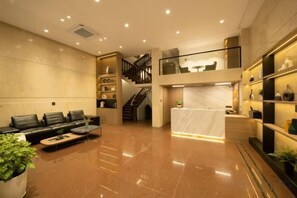 Vestíbulo de hotel con mostrador de recepción, zona de estar, escalera y estanterías decorativas.