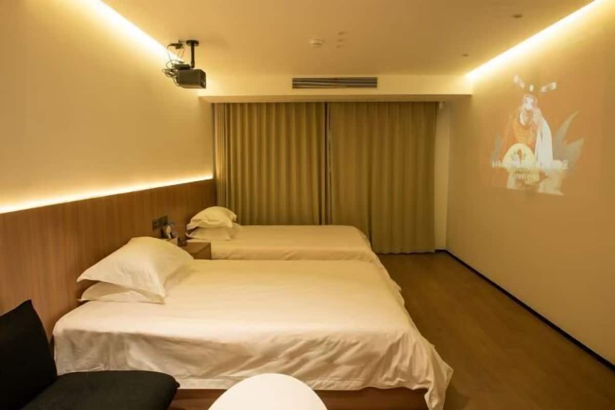A hotel room with two beds, a sofa, a projector on the wall, and a curtain.