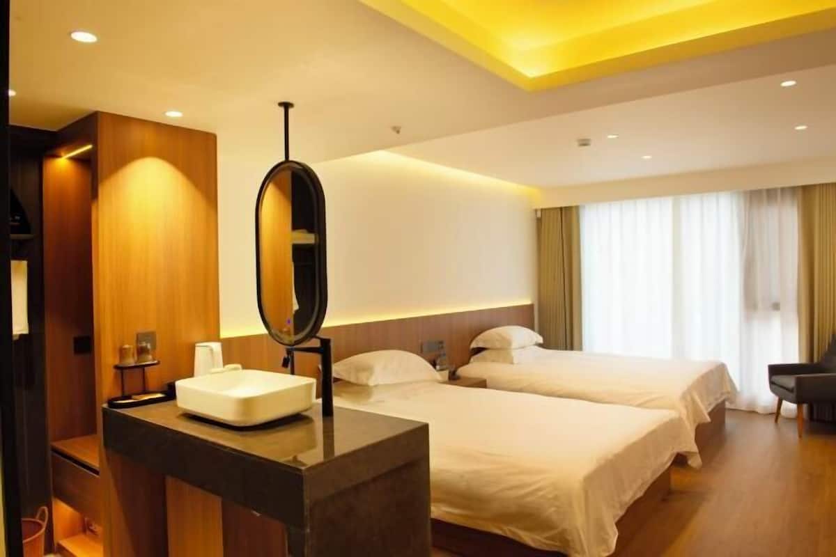 A hotel room with a bed, a bedside table, a mirror, and a window with curtains.