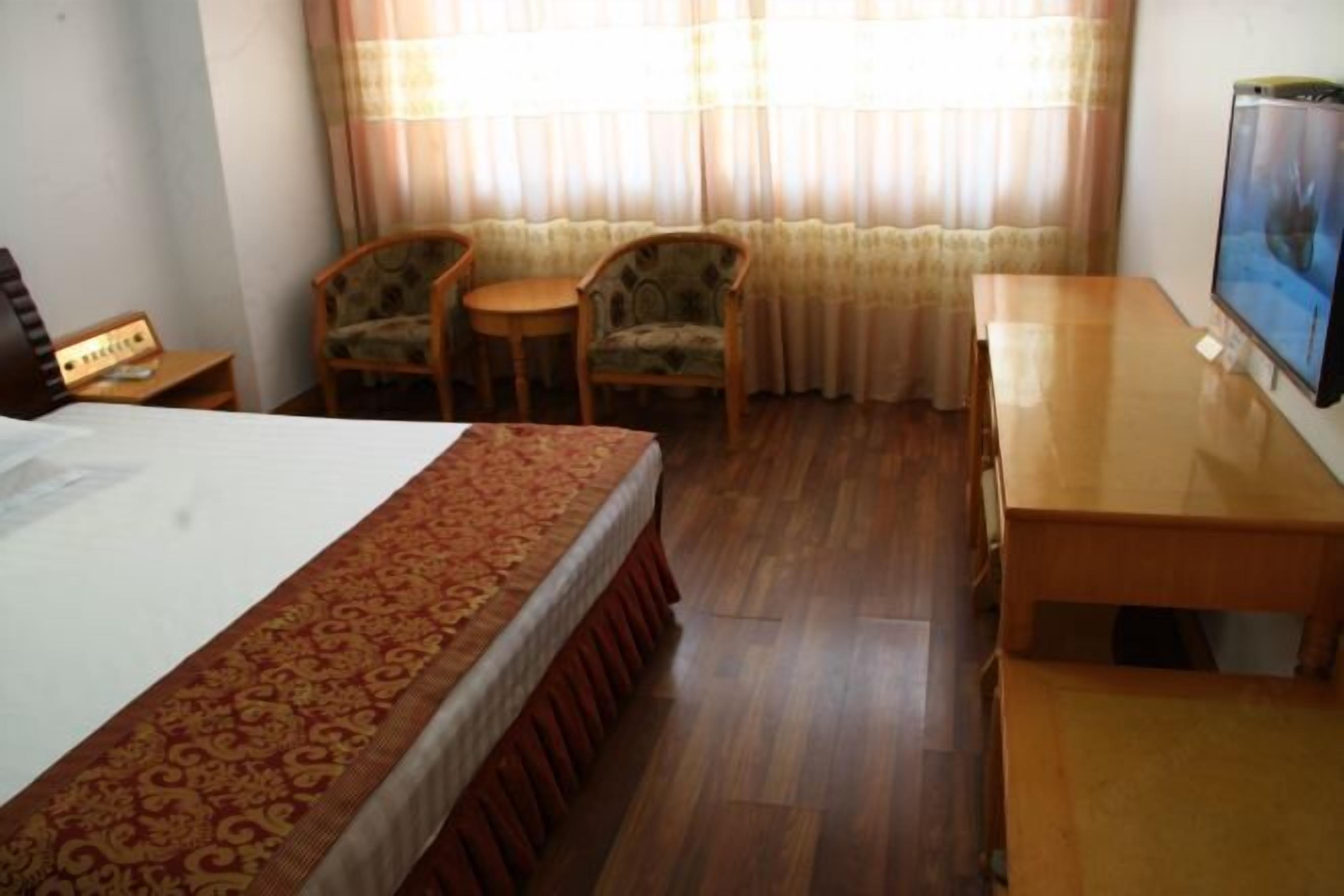 A hotel room with a bed, a desk, two chairs, a small table, and a television.