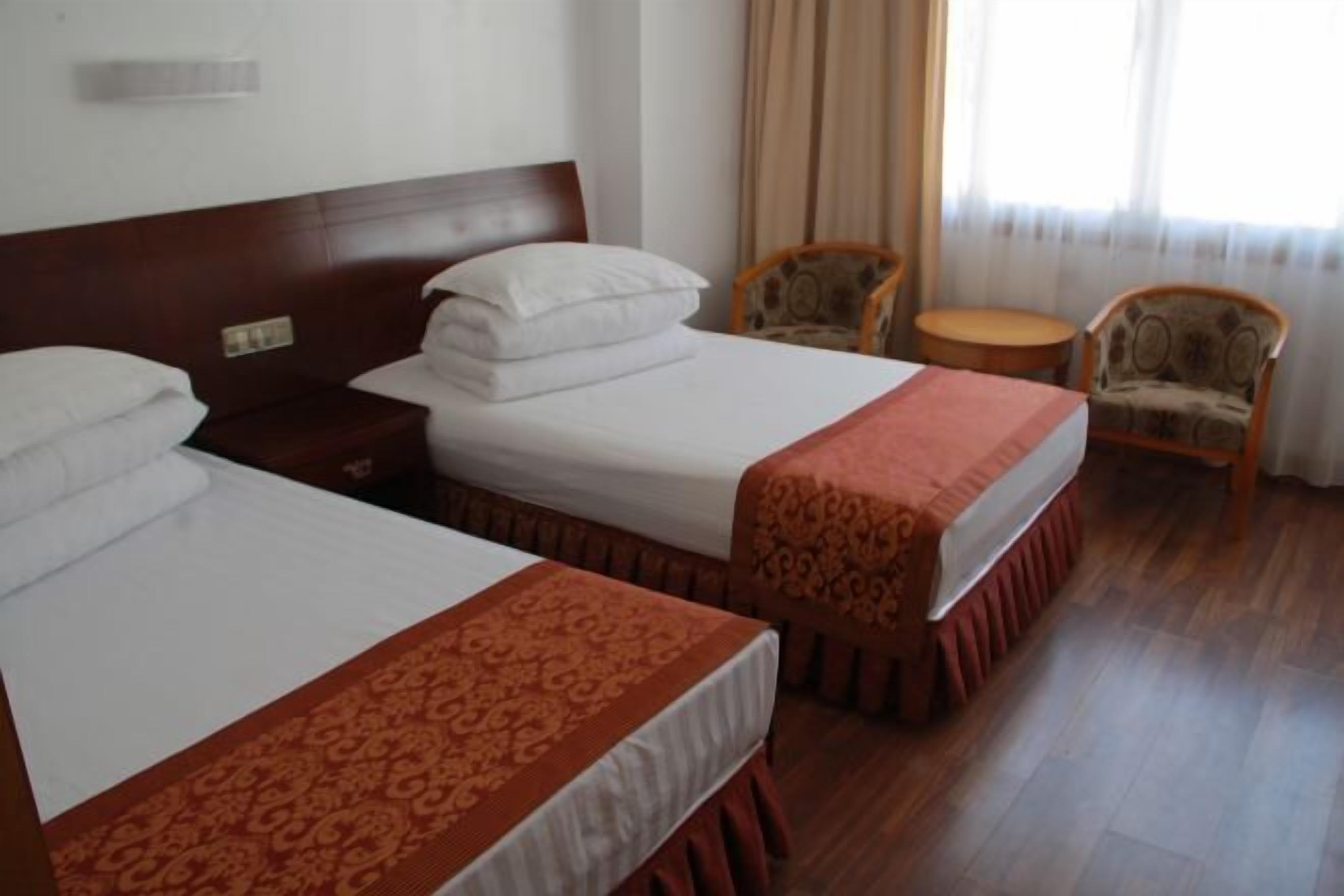 A hotel room with two beds, a wooden headboard, a small round table, and two patterned chairs.