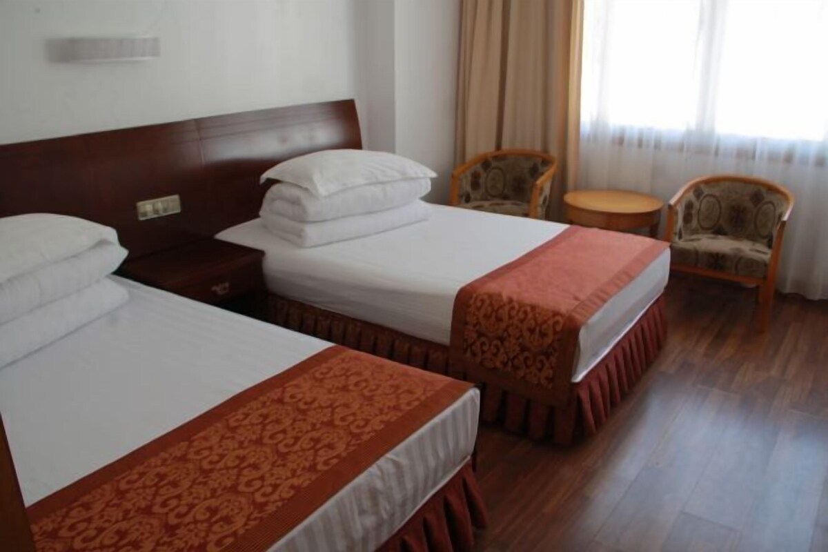 A hotel room with two beds, a wooden headboard, a small round table, and two patterned chairs.