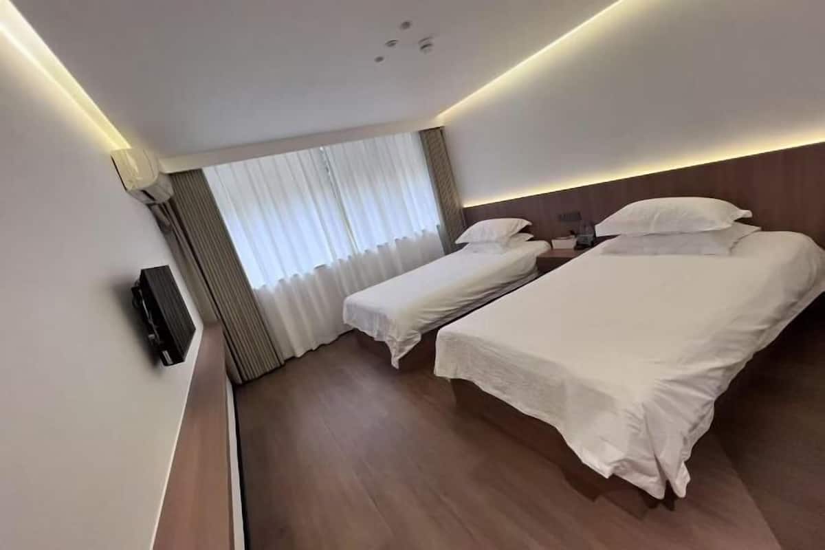 A hotel room with two beds, a flat-screen TV, a window with curtains, and a wooden floor.