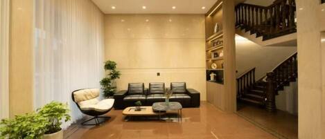 A spacious living area with a sofa set, a coffee table, and potted plants. A staircase is visible in the background.
