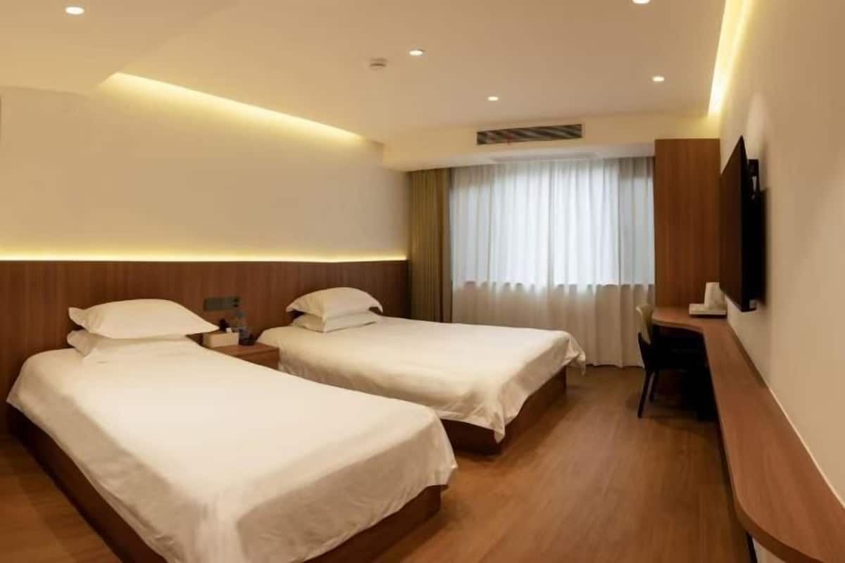 A hotel room with two beds, a desk, a chair, a TV, and a window with curtains.
