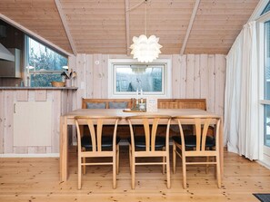 A wooden interior with a dining table, chairs, a window with a view, and a hanging light fixture.