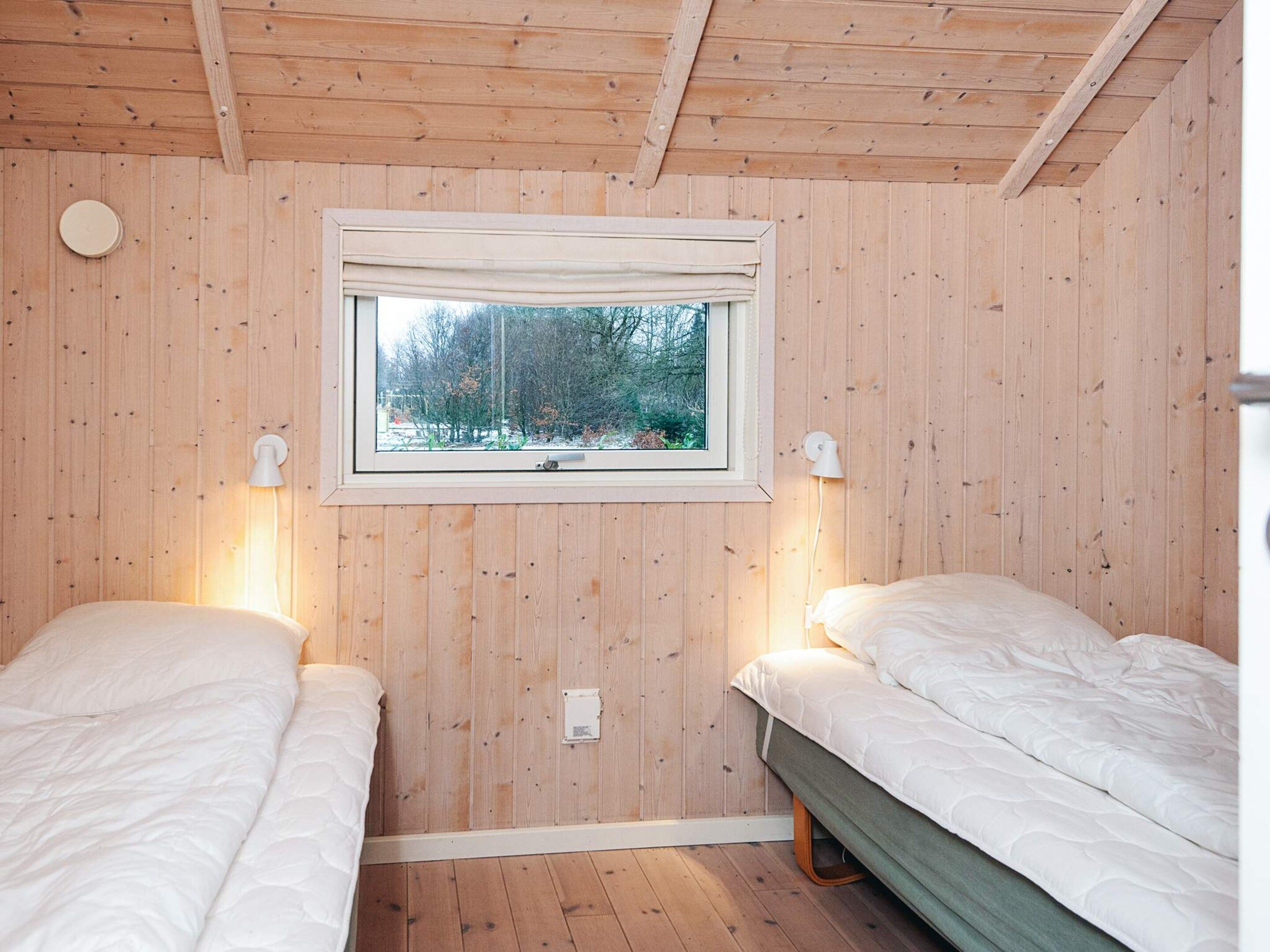 A room with two beds, wooden walls, a window, and two wall-mounted lamps.