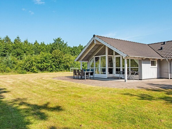 A house with a covered patio, a lawn, and a forest in the background.