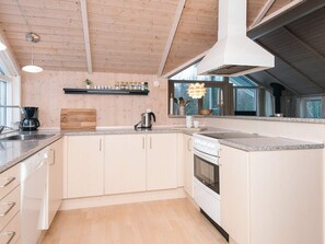 A modern kitchen with wooden beams, a built-in stove, and a large window.