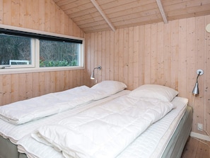 A room with wooden walls, a window, two beds with white bedding, and two wall-mounted lamps.